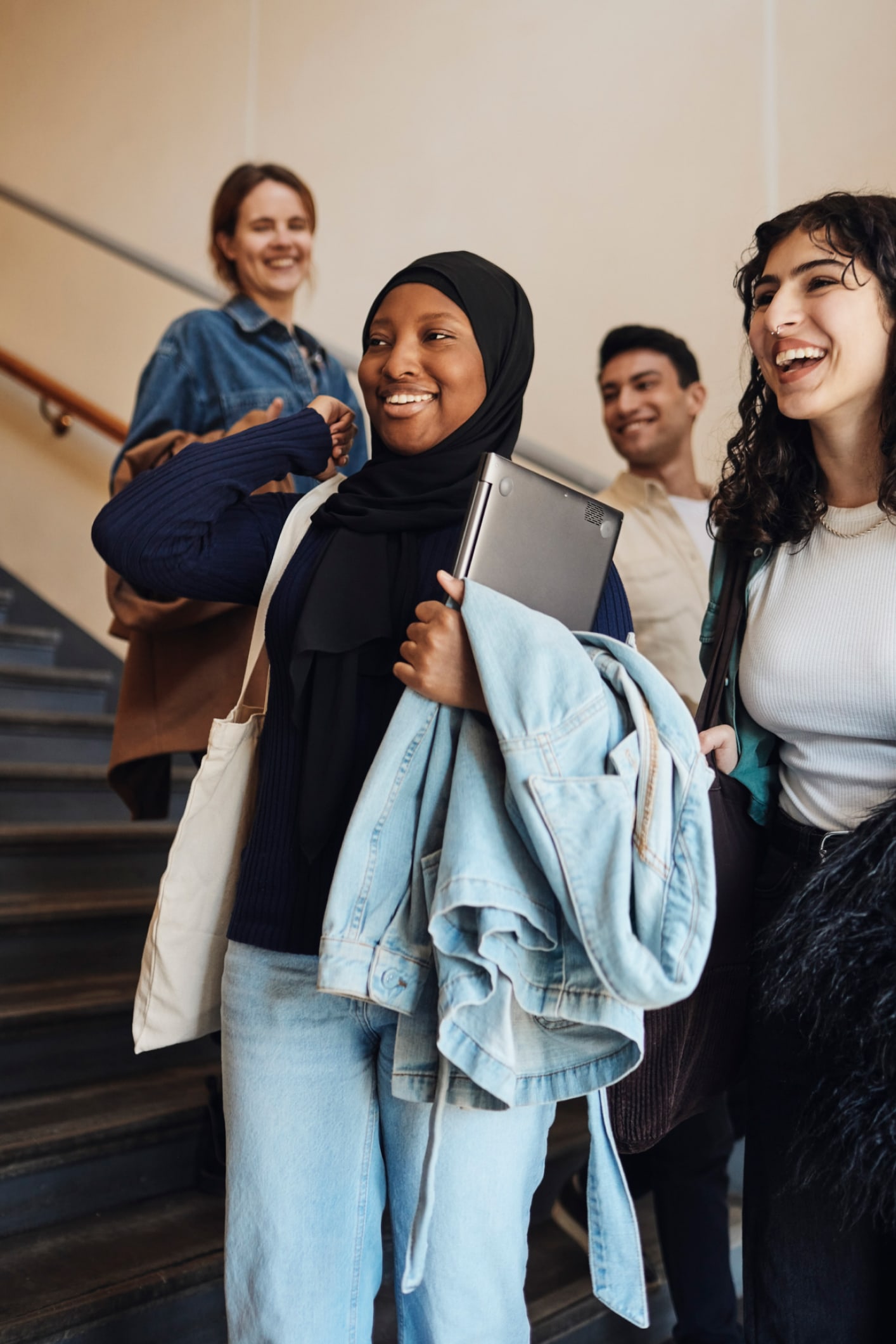 Mulher sorridente de hijab segura um laptop enquanto desce as escadas
